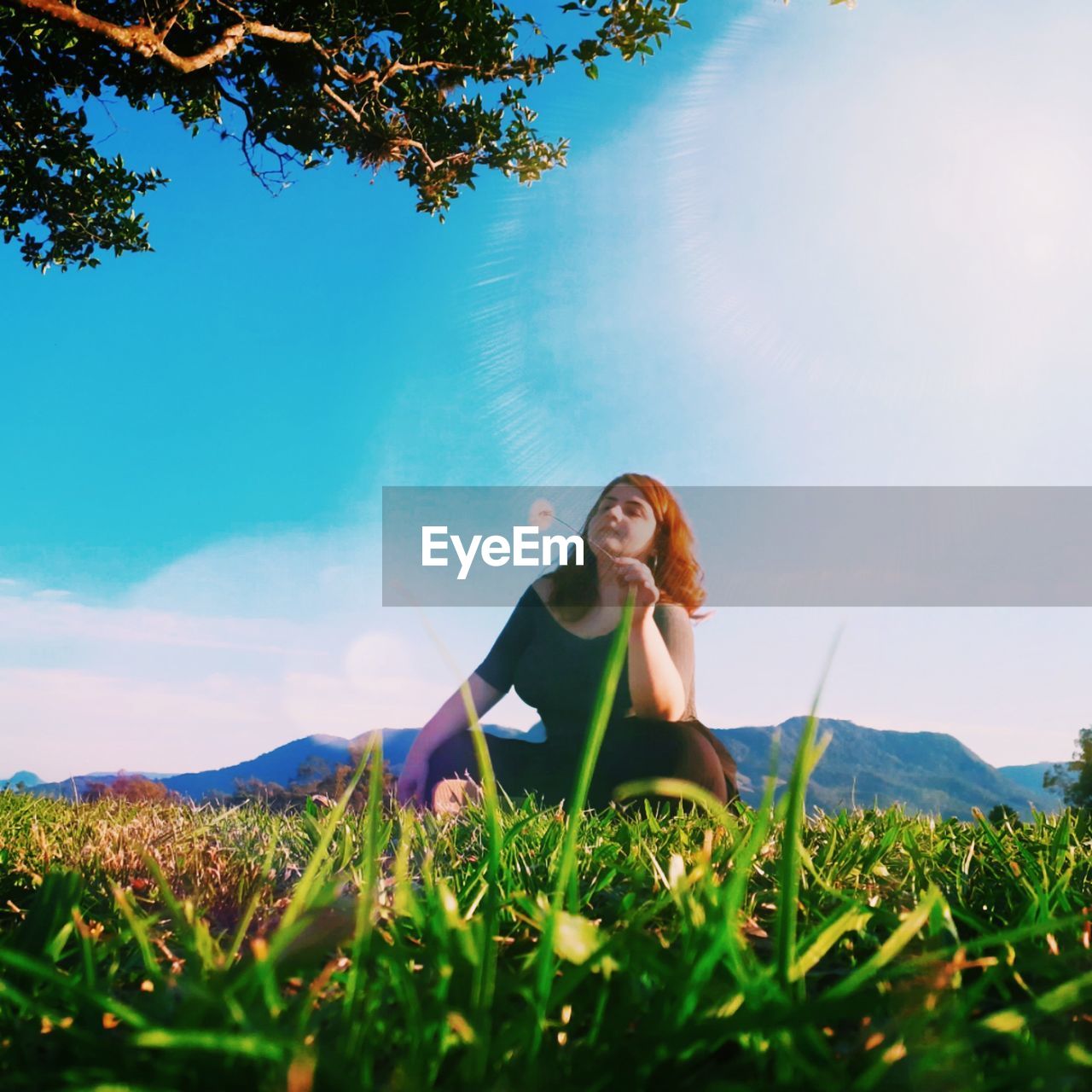 Low angle view of woman sitting on grassy land against sky