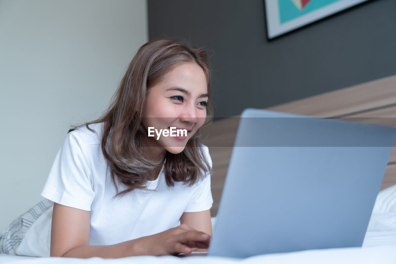 PORTRAIT OF A SMILING YOUNG WOMAN USING LAPTOP