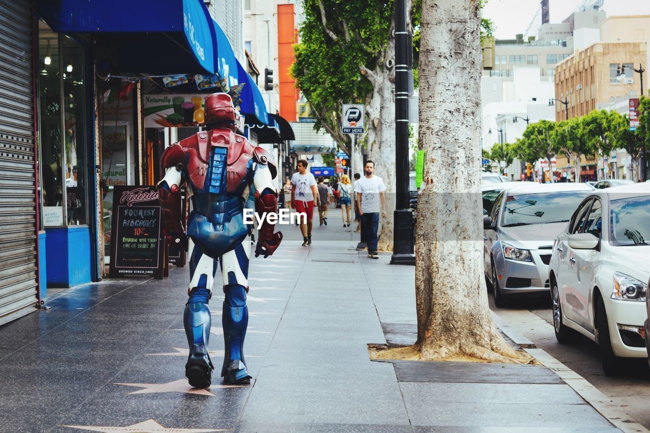 Rear view of man wearing metal costume while walking on sidewalk