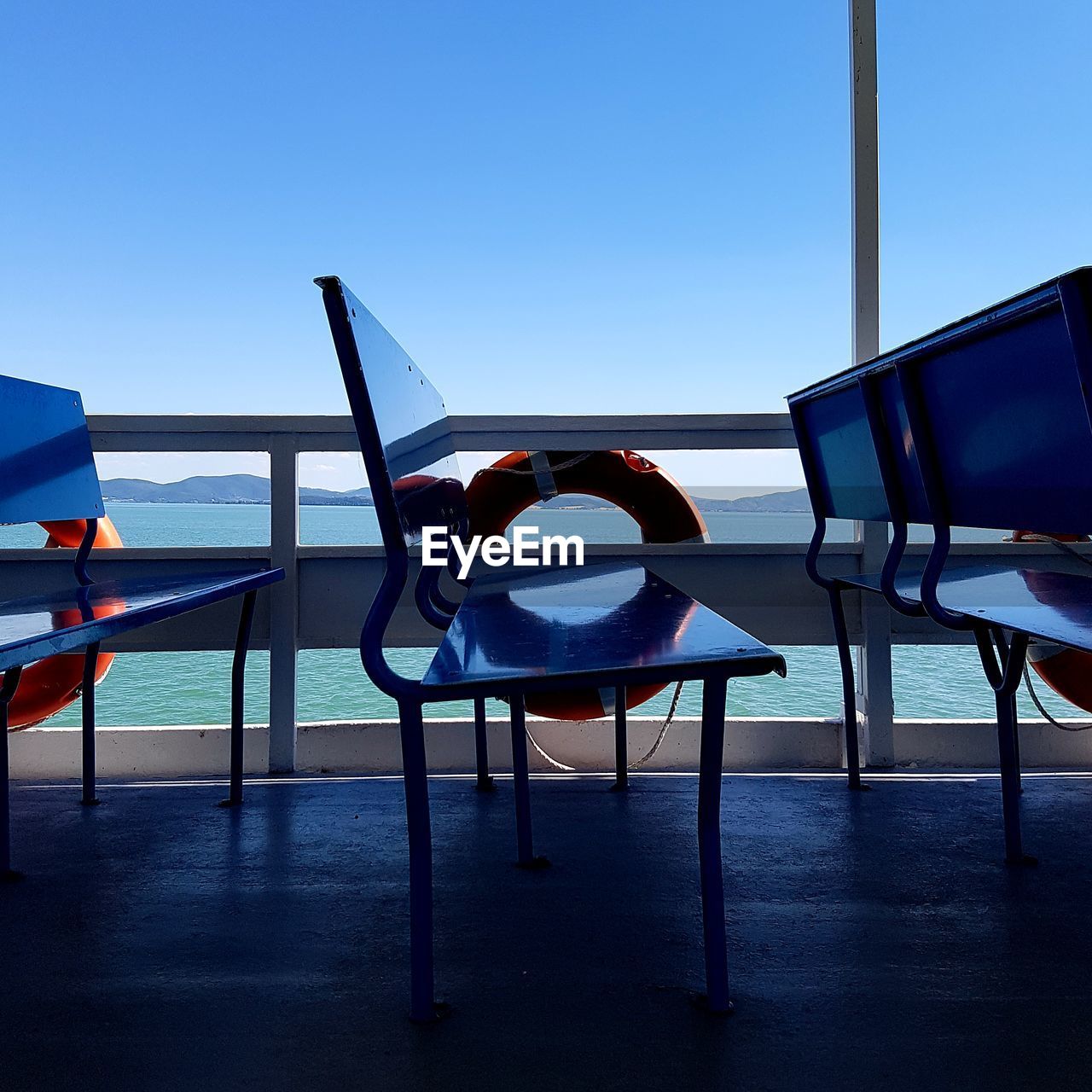 EMPTY CHAIRS AND TABLE AT BEACH AGAINST CLEAR SKY