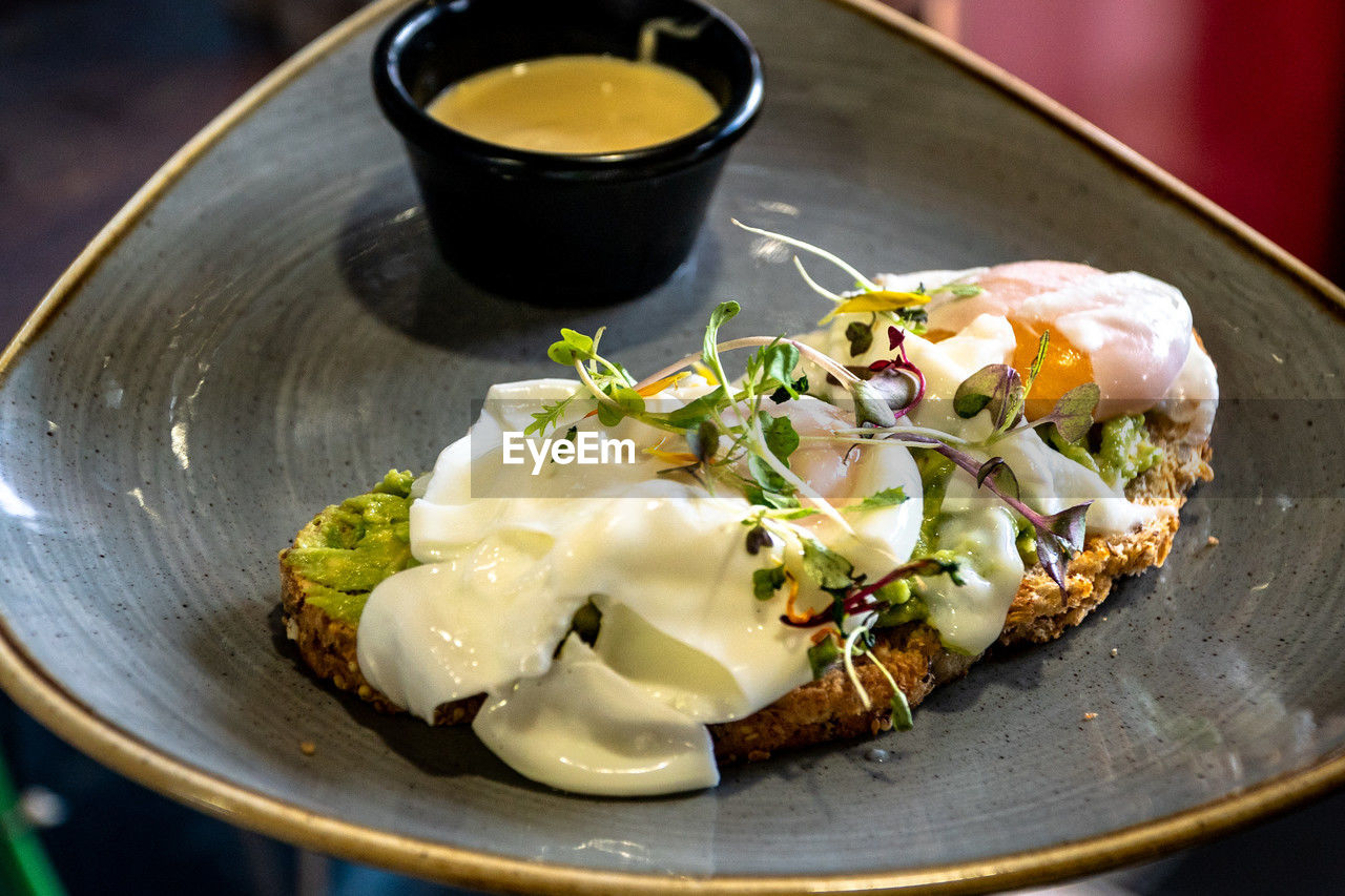 A slice of avocado toast topped with poached eggs and hollandaise sauce.