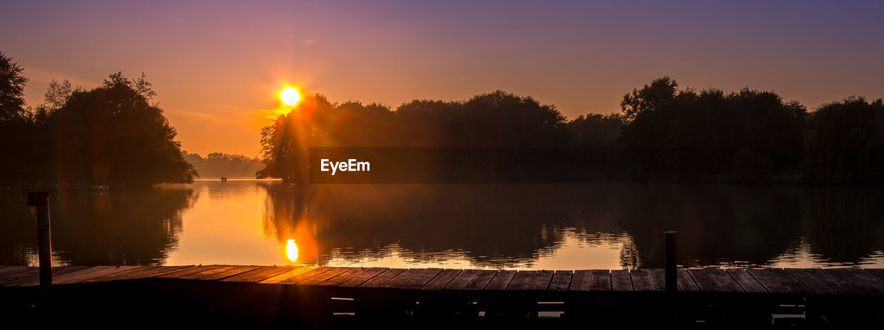 REFLECTION OF TREES IN WATER AT SUNSET