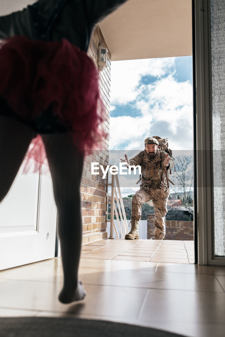 Low angle of surprised daughter running towards father returning from military service standing in doorway