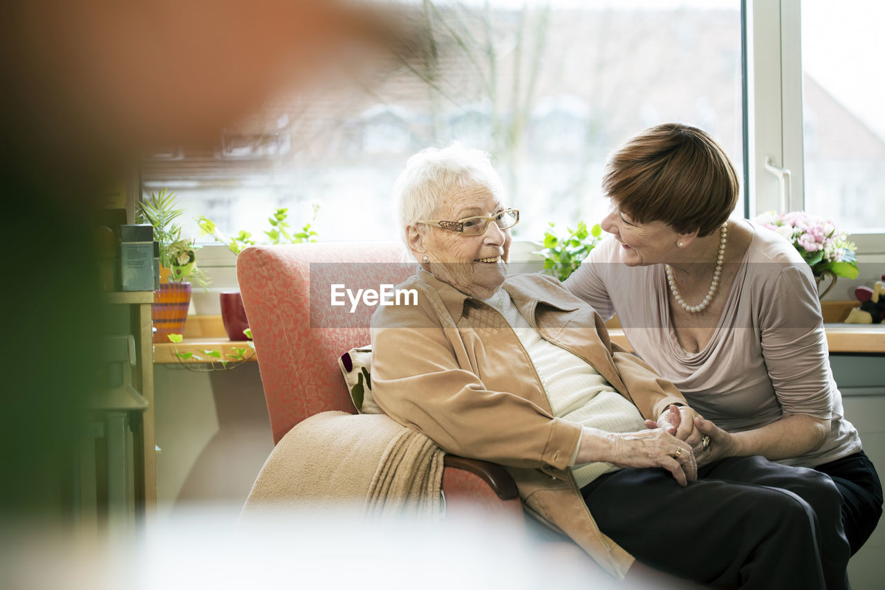 Adult daughter talking to her mother with alzheimer's disease in her room at retirement home