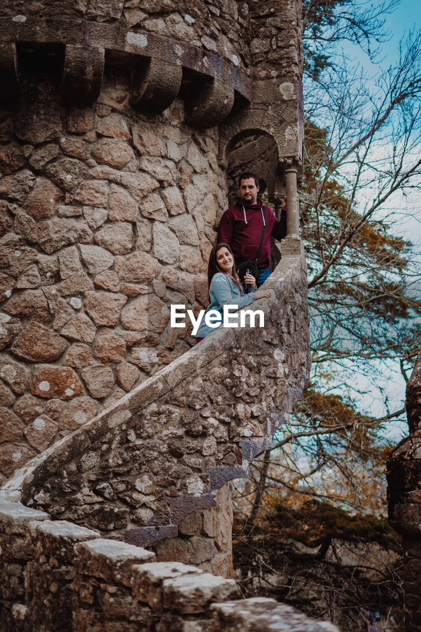 Couple standing by retaining wall in tower against sky