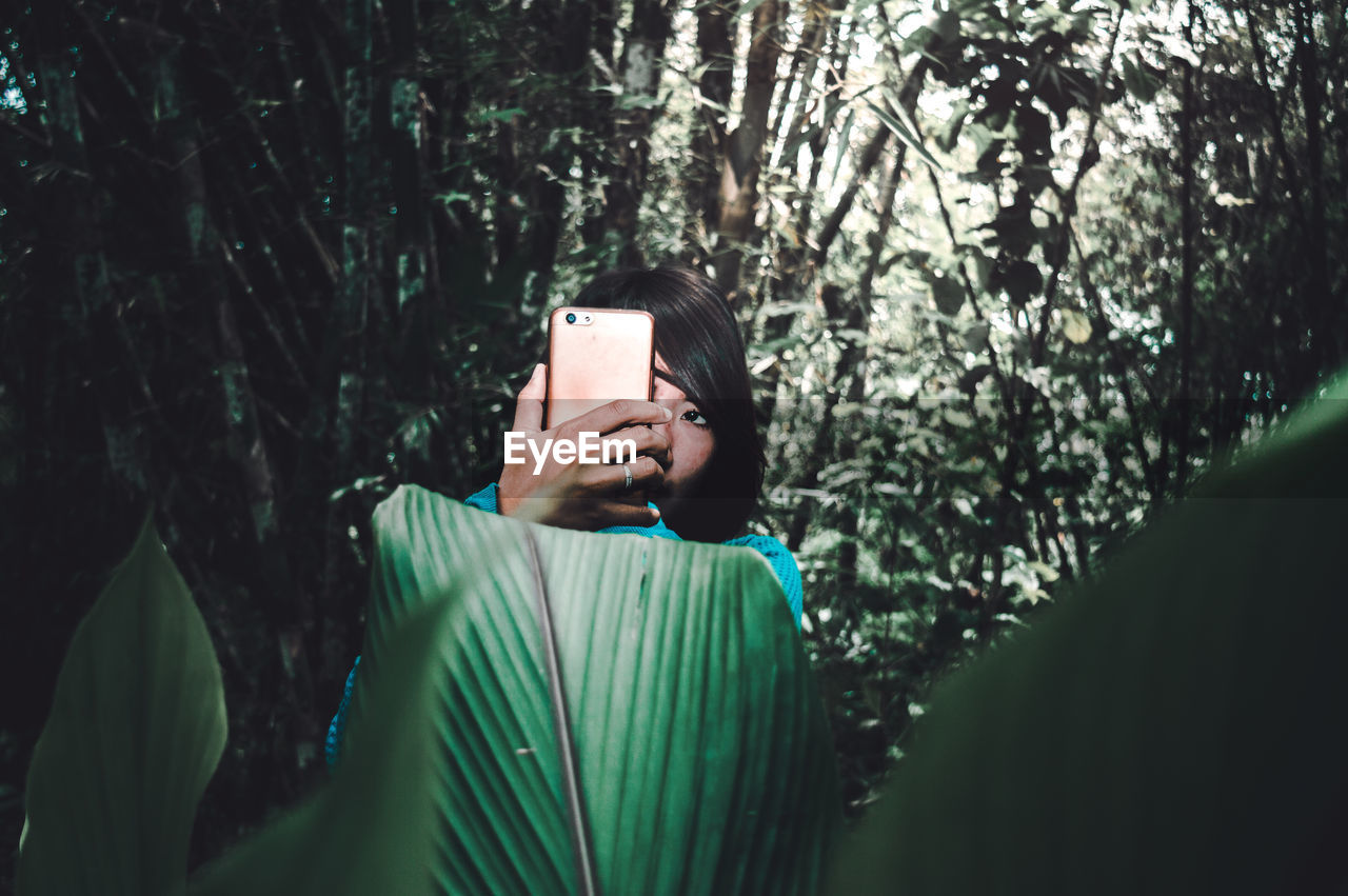 Woman photographing with smart phone in forest