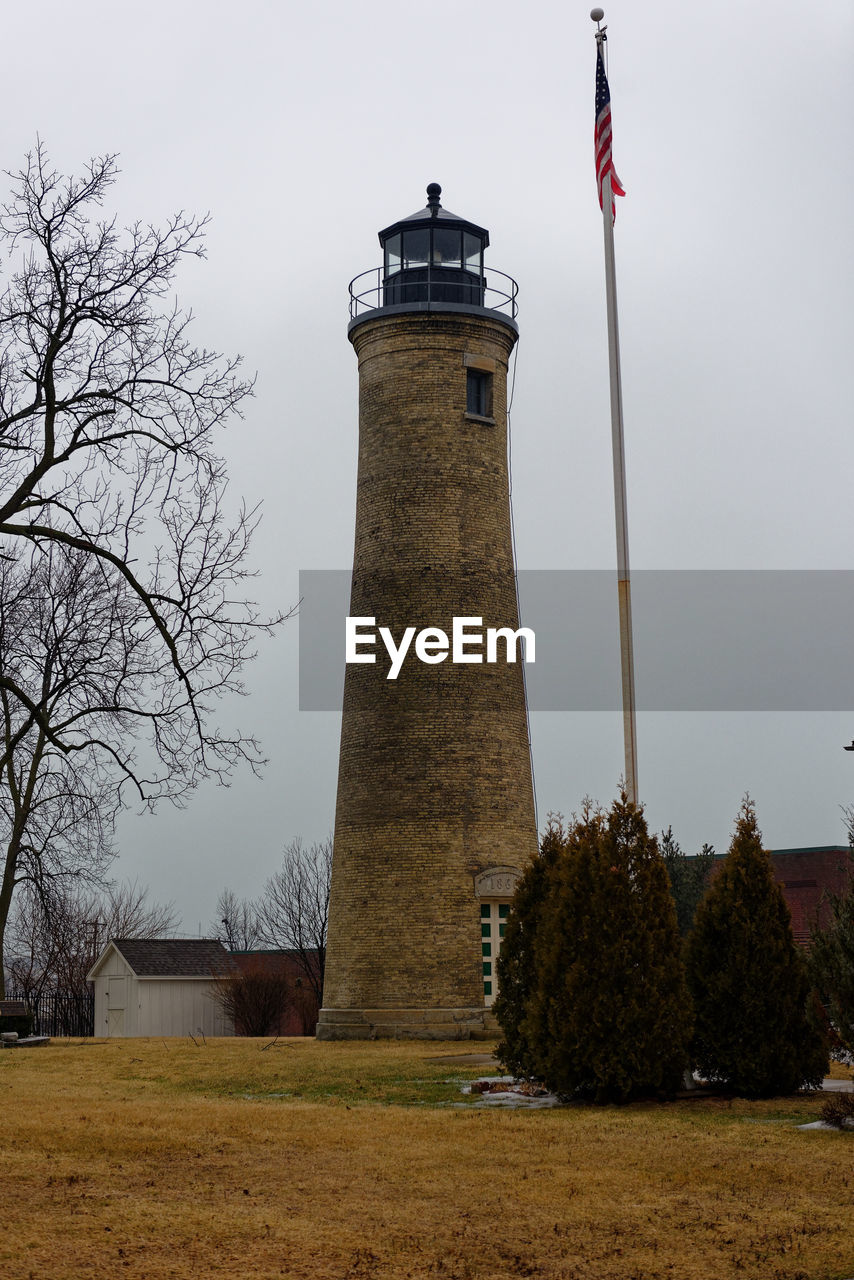 Lighthouse on field by building against sky