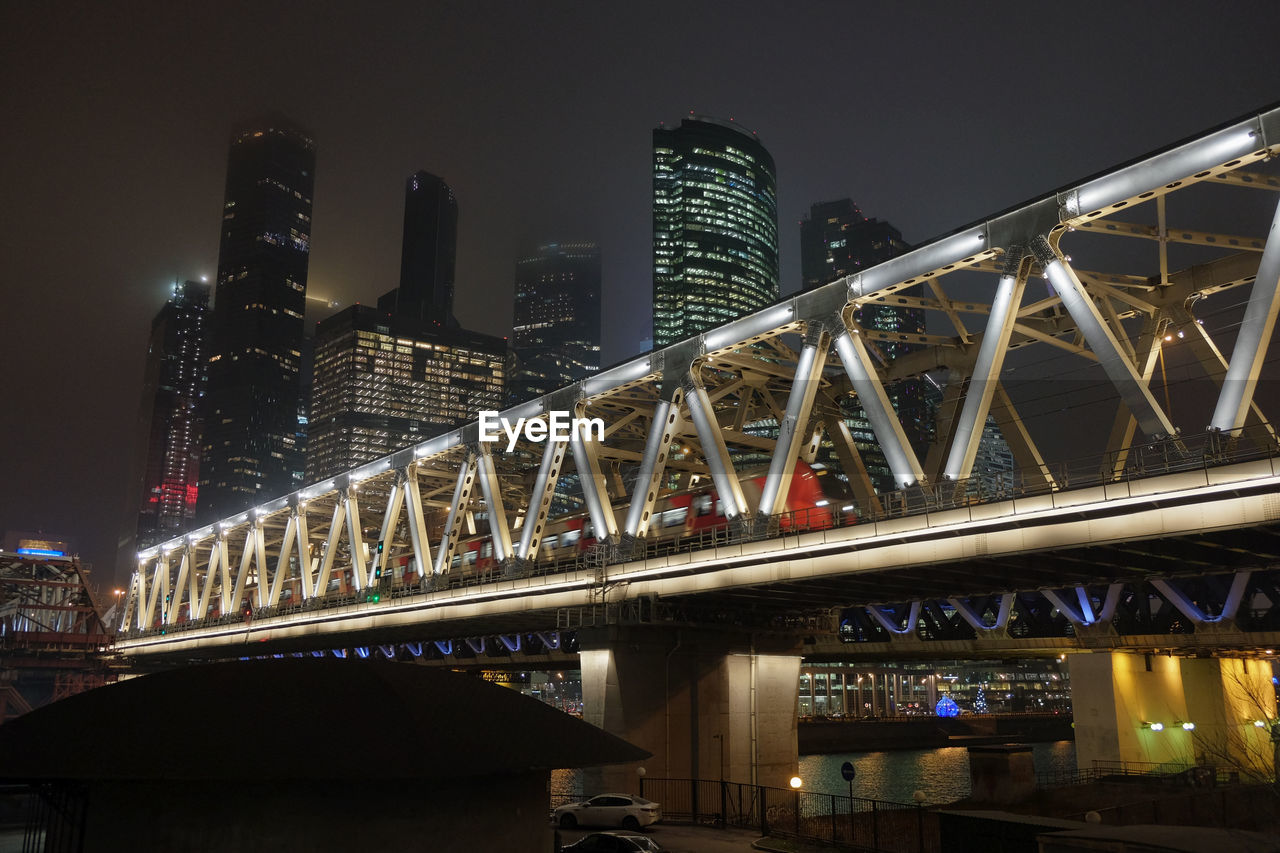 LOW ANGLE VIEW OF ILLUMINATED BRIDGE BY BUILDINGS AGAINST SKY