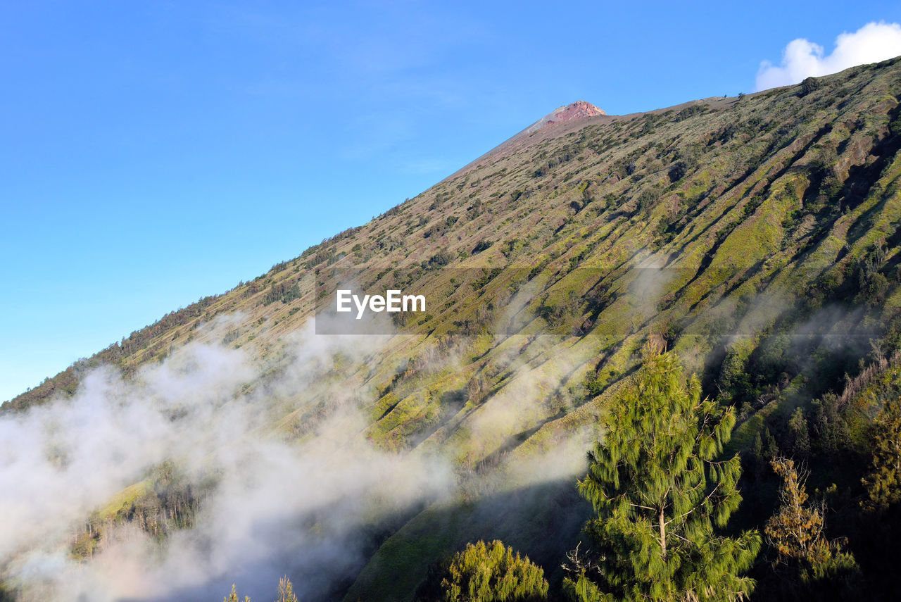 Low angle view of volcanic mountain against clear blue sky