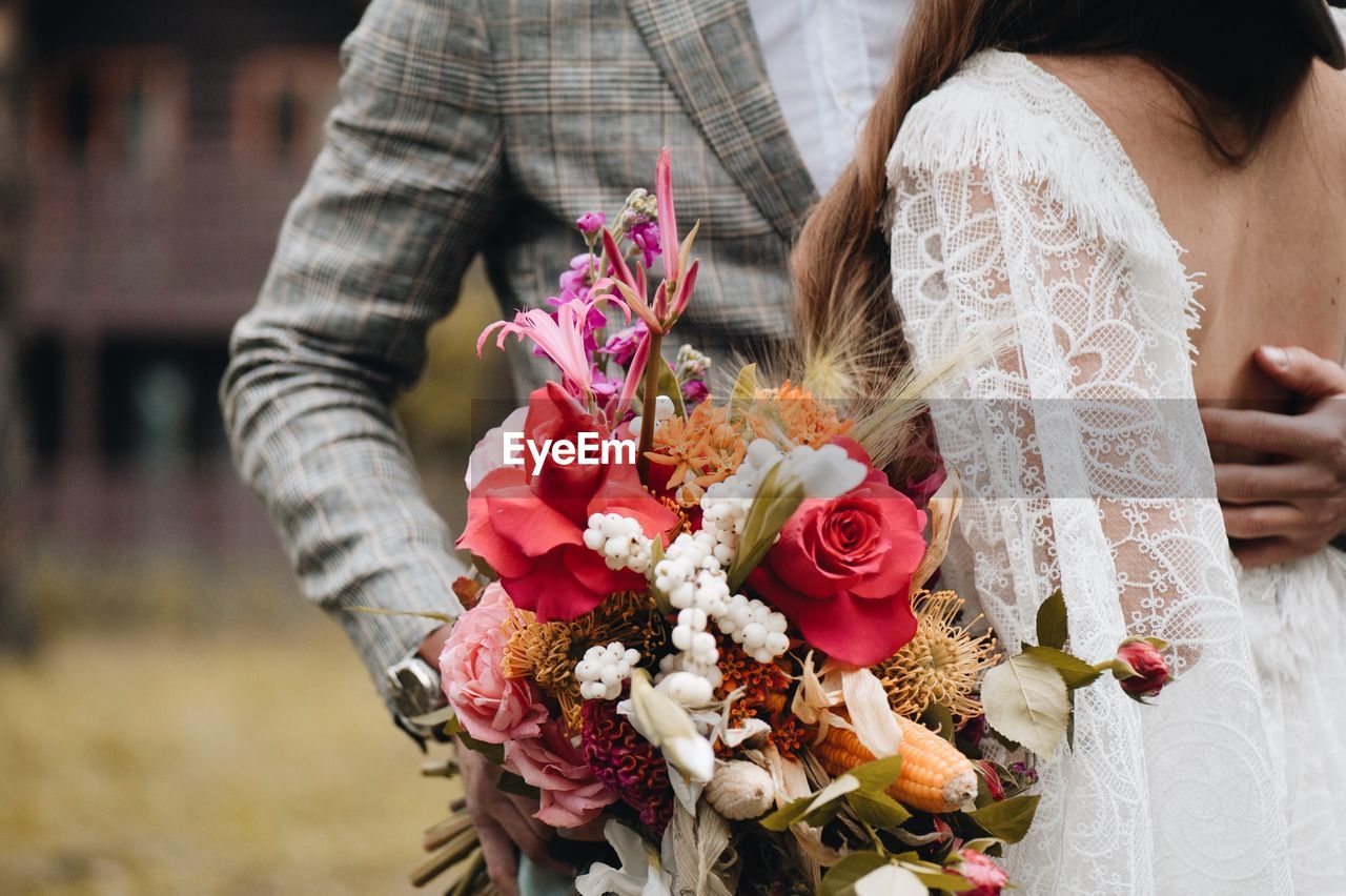 Midsection of couple holding bouquet while standing outdoors