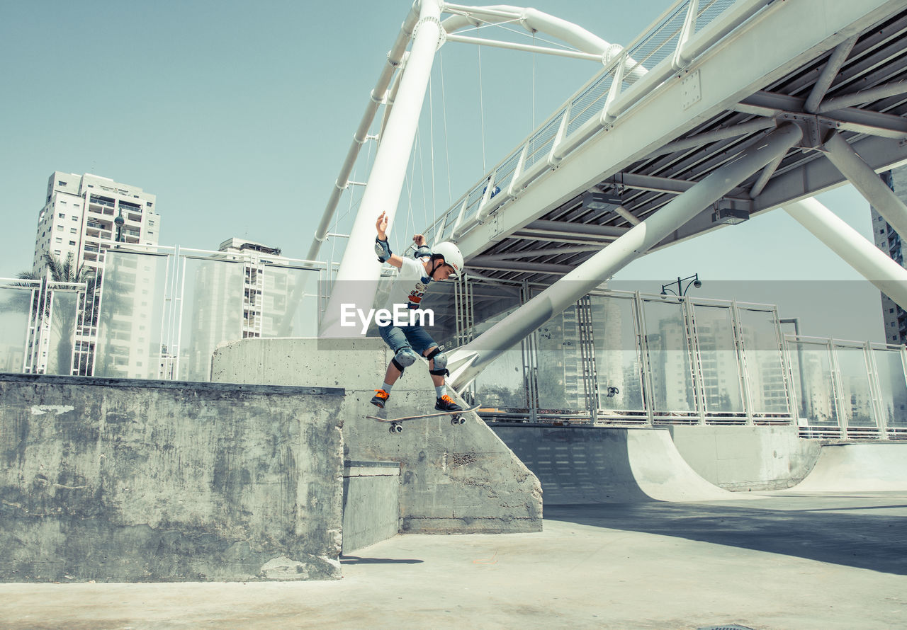 Boy performing stunt while skateboarding in park against clear sky