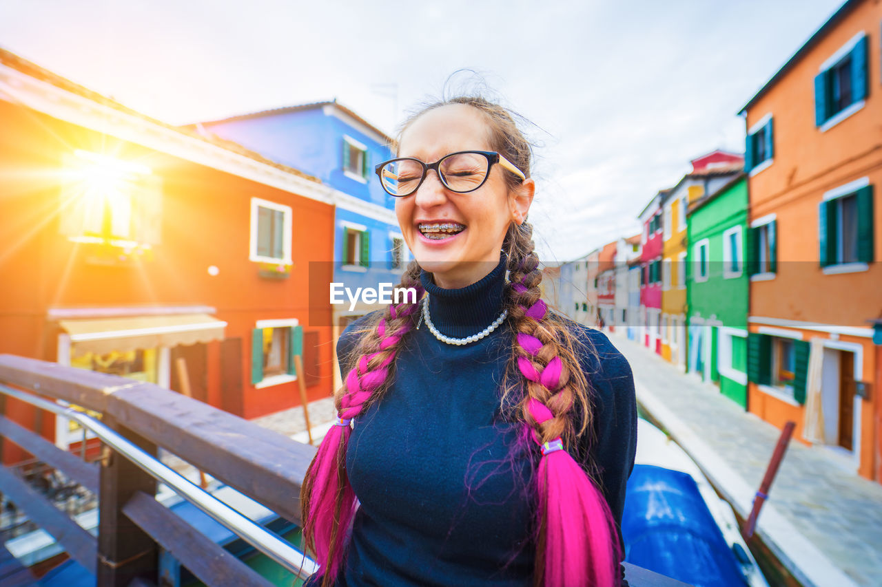 portrait of smiling young woman standing against built structures