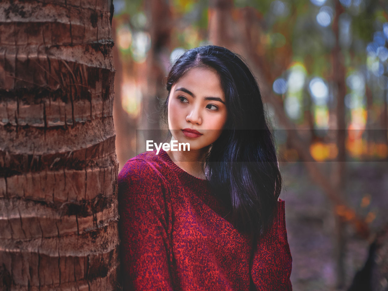 Portrait of young woman standing against tree