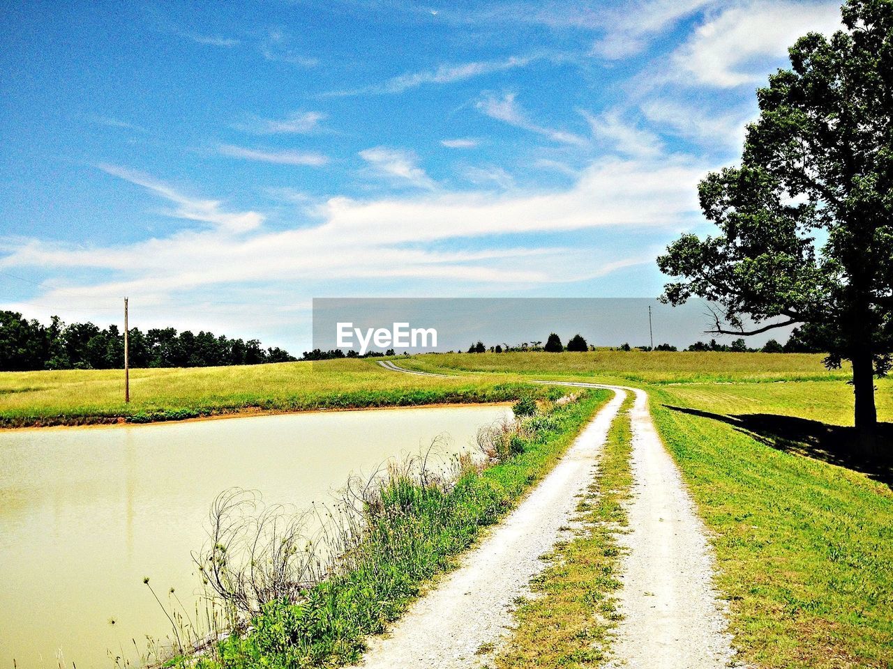 Pathway by lake on field against sky