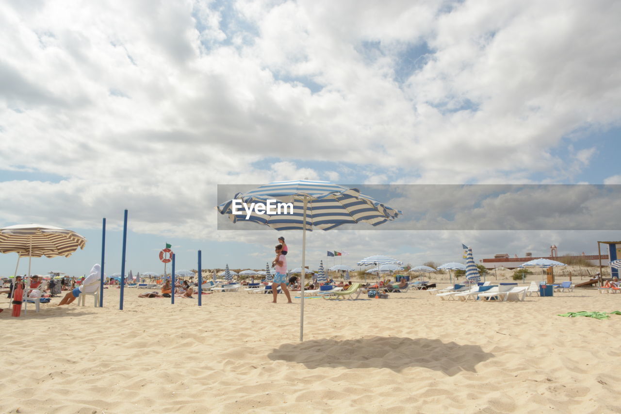 People enjoying at beach against cloudy sky