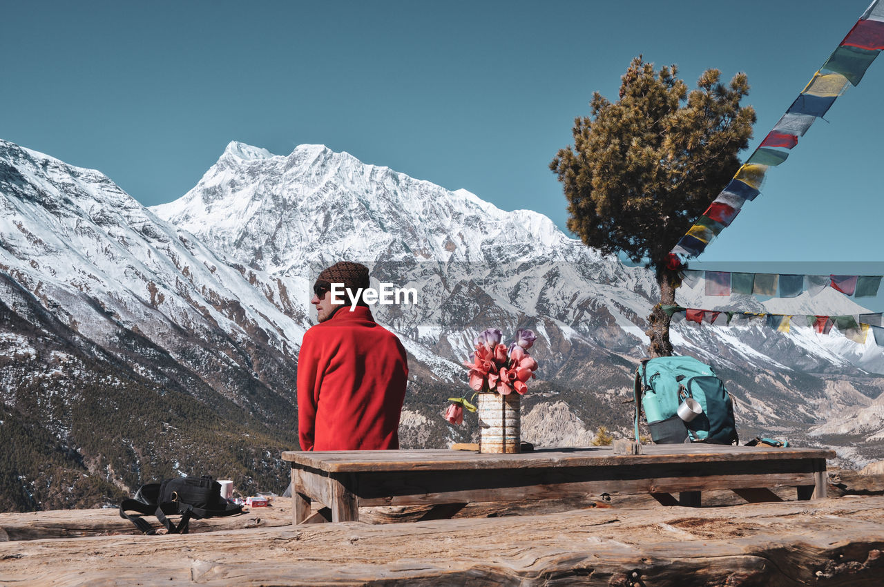 Rear view of man sitting against snowcapped mountains