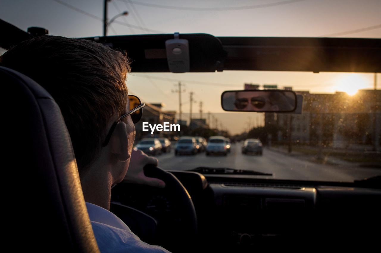 Young man driving car on street at dusk