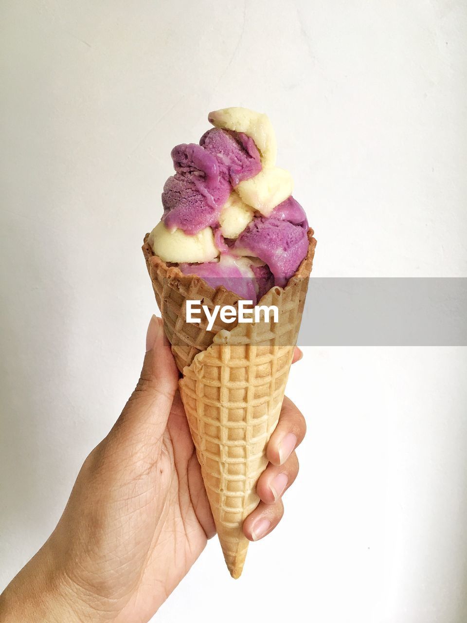 CLOSE-UP OF HAND HOLDING ICE CREAM CONE ON WHITE BACKGROUND