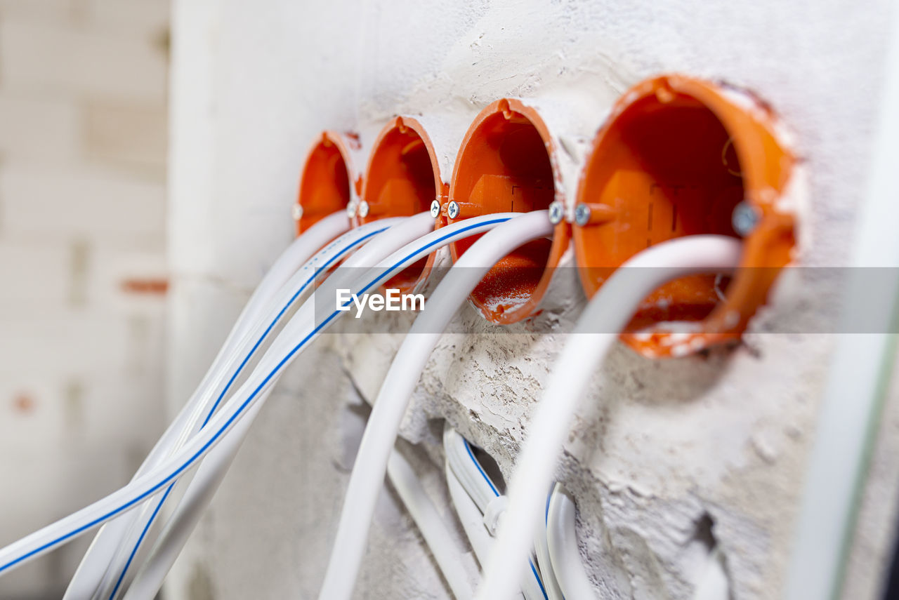 Orange, round junction box mounted in the white wall with protruding electric cables.