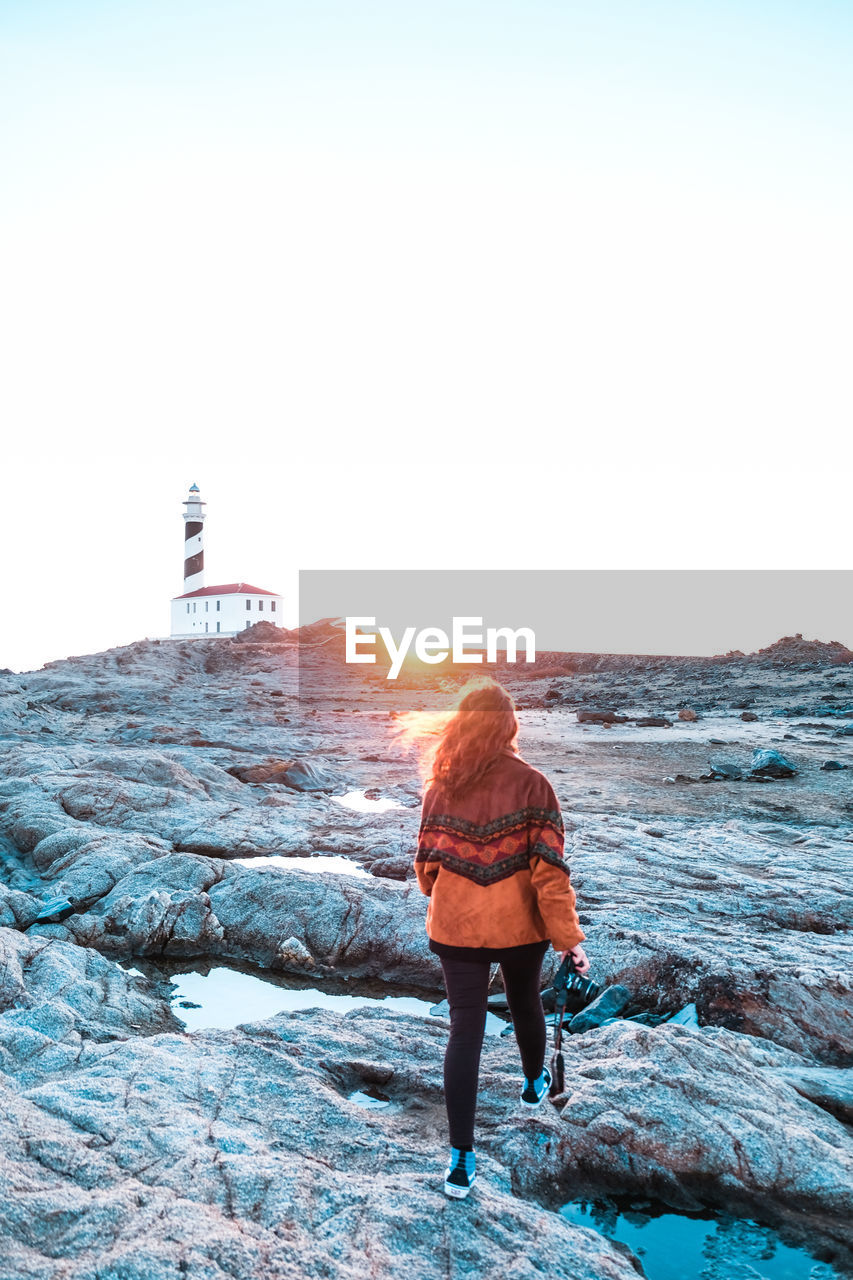 Rear view of woman walking on rock at beach against sky