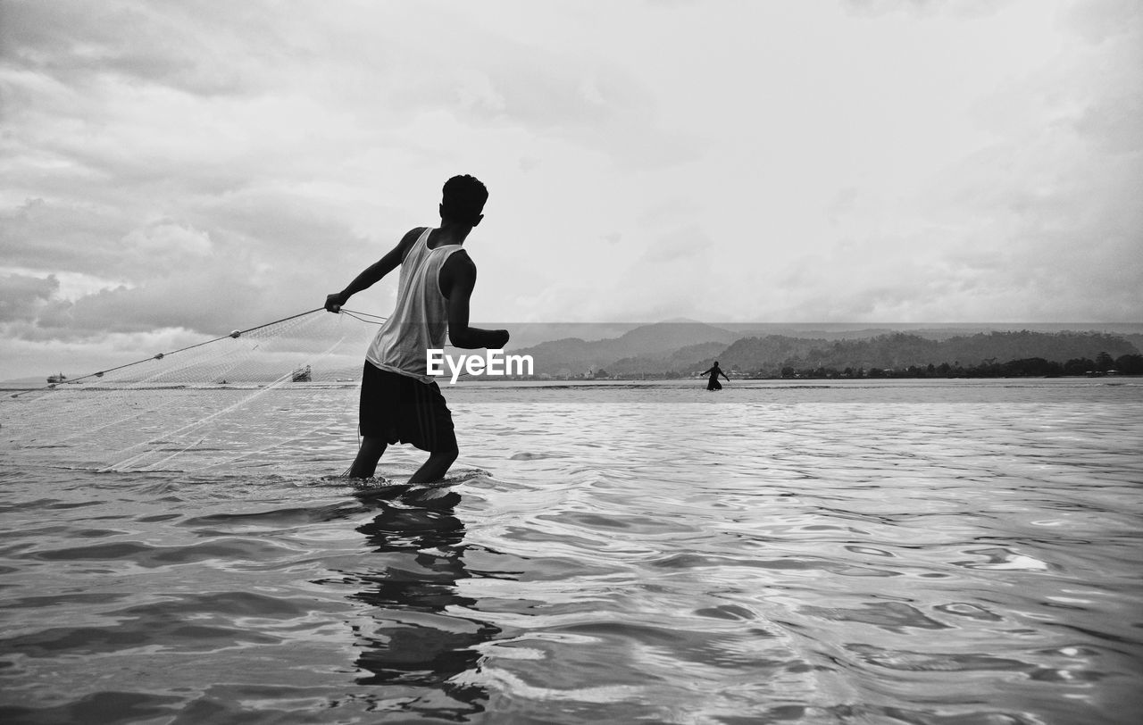 Rear view of man standing in sea against sky