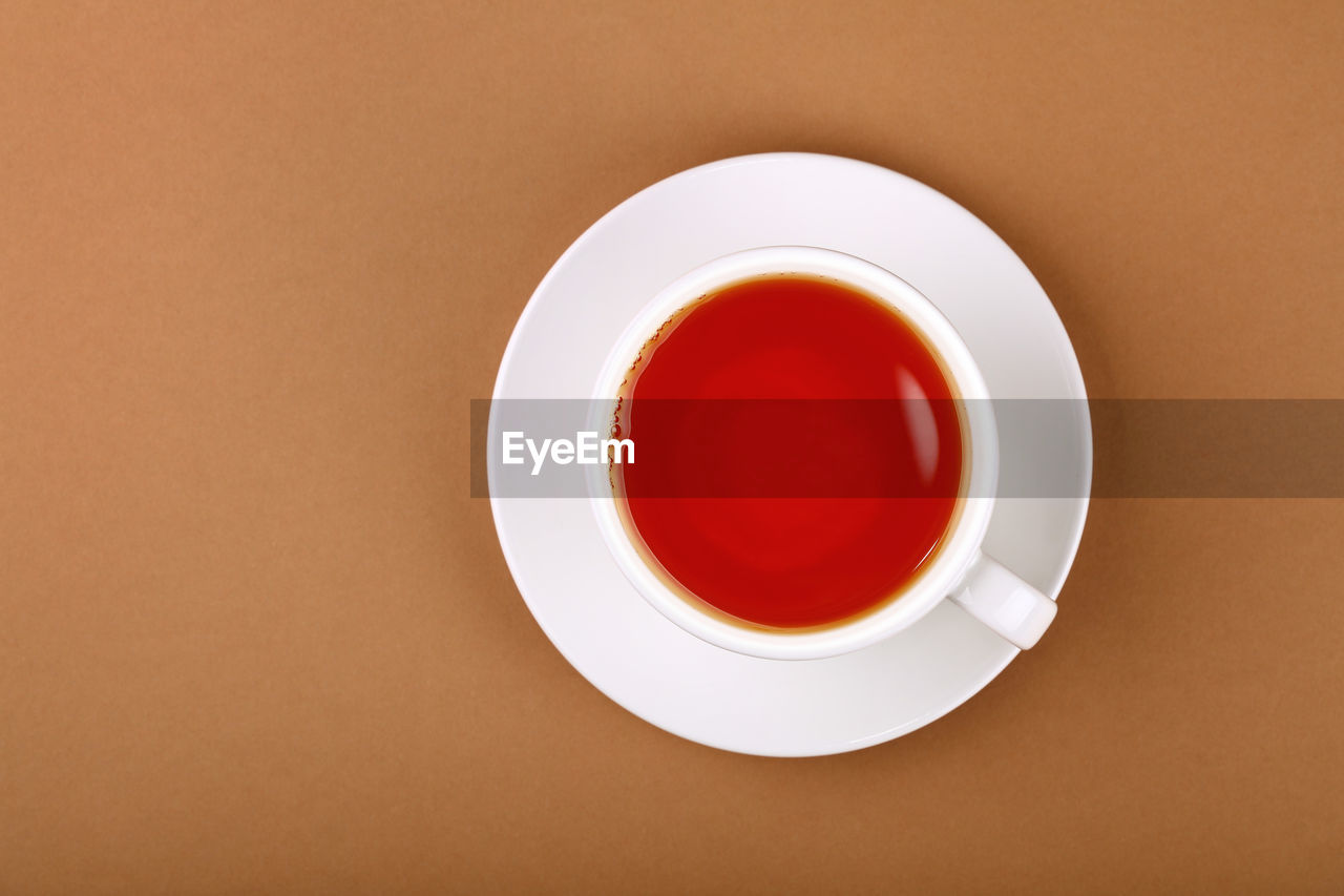 Close up one cup full of red black or fruit tea on white saucer over brown paper, elevated top view