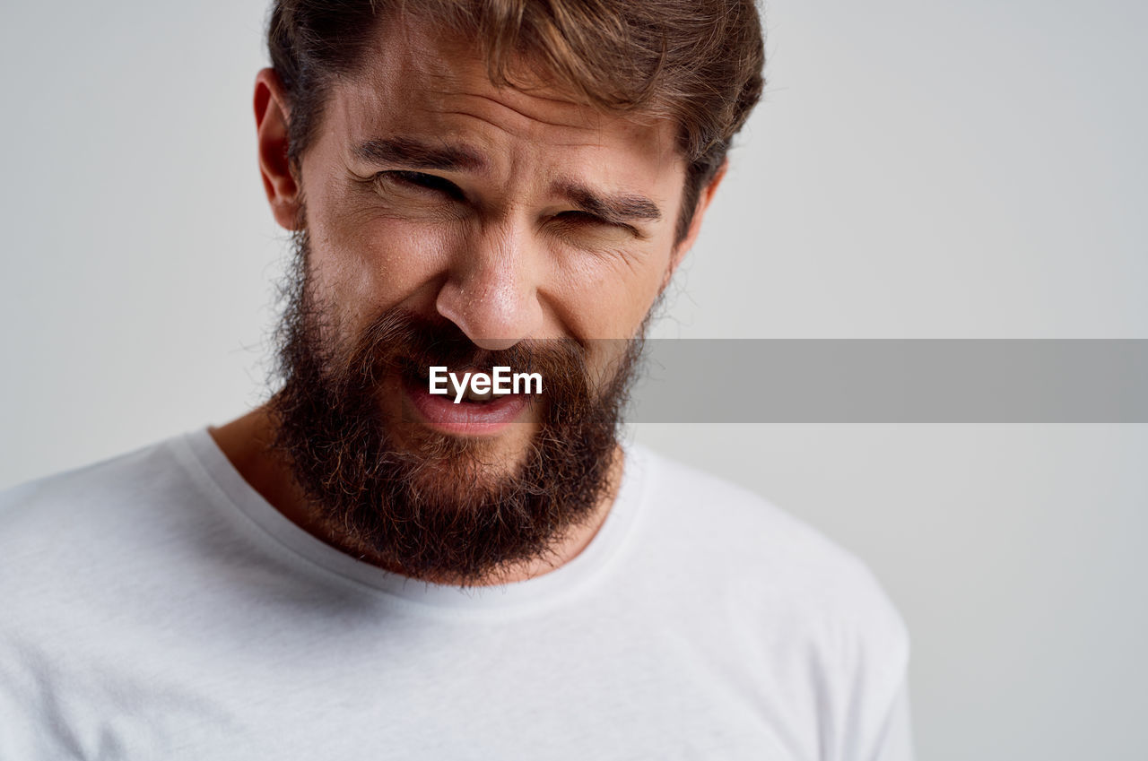 facial hair, beard, human hair, one person, portrait, studio shot, adult, headshot, moustache, hairstyle, indoors, emotion, men, casual clothing, gray, front view, smiling, happiness, gray background, brown hair, human face, young adult, person, t-shirt, facial expression, close-up, human head, teeth, nose, positive emotion, copy space, smile, eyes closed, white background, lifestyles