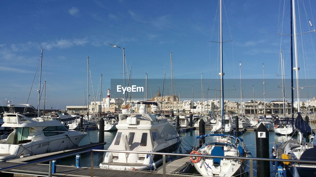 Boats moored at harbor against blue sky