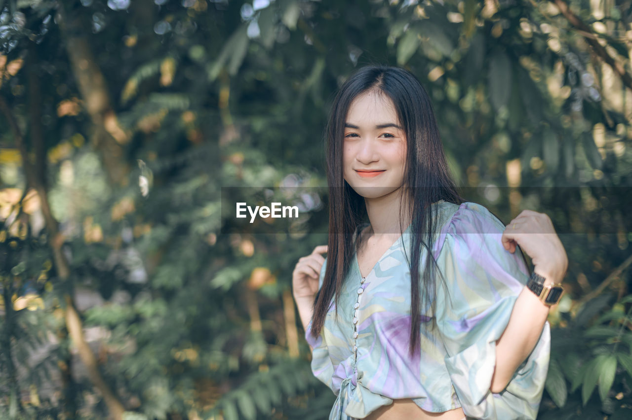 Portrait of smiling young woman standing against trees