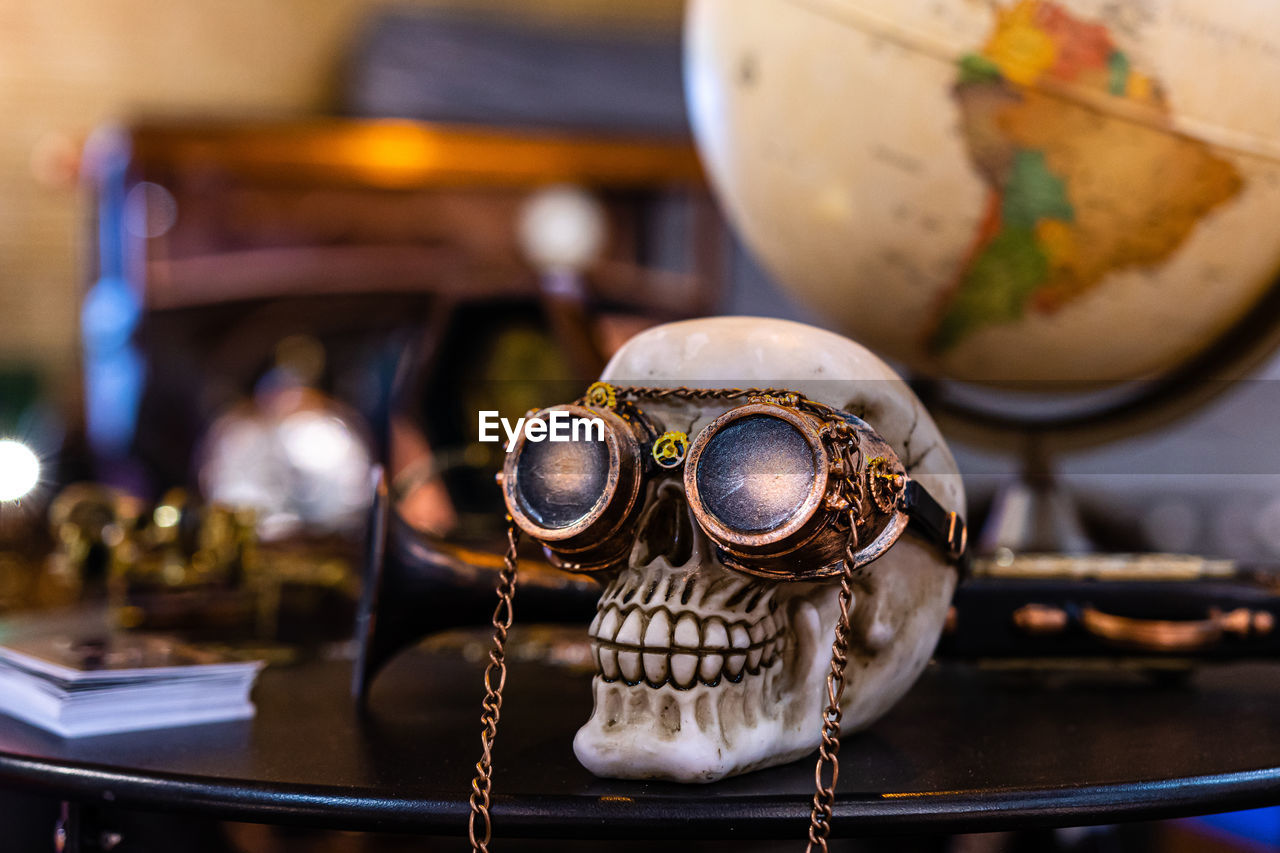 Skeleton head with steampunk glasses on defocused background with globe and old car - image