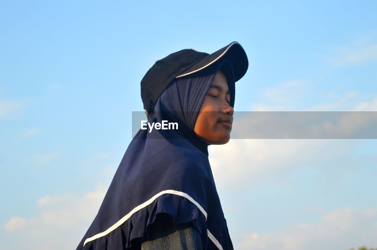 Low angle view of woman wearing cap standing against sky