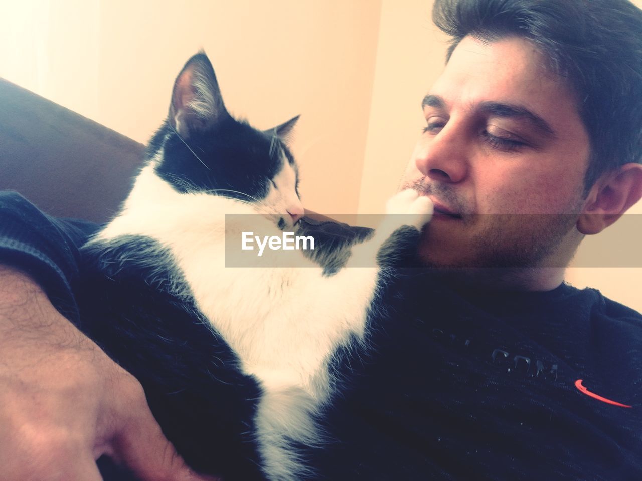 domestic animals, pet, mammal, animal, animal themes, one animal, cat, nose, one person, beard, adult, men, skin, facial hair, indoors, domestic cat, relaxation, young adult, home interior, friendship, lifestyles, love, dog, black, smiling, happiness, canine, positive emotion, feline, portrait, casual clothing, emotion, person, whiskers, furniture, affectionate, leisure activity, blue, looking, headshot