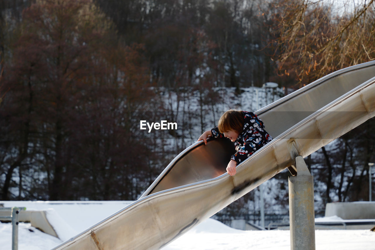 Boy playing on slide over snow covered playground