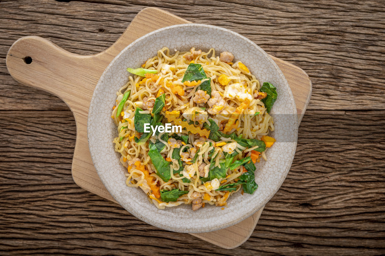 Stir fried instant noodles with pork, egg, chinese kale, carrot and pepper in crazing ceramic plate