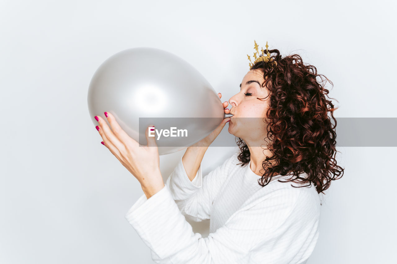 Woman blowing balloon while standing against white backgrounds