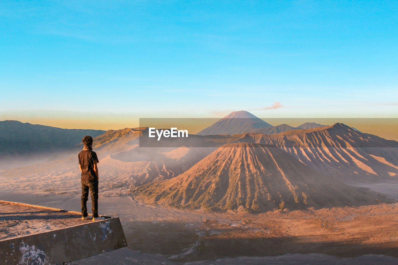 Man standing at observation point against mountains during sunset