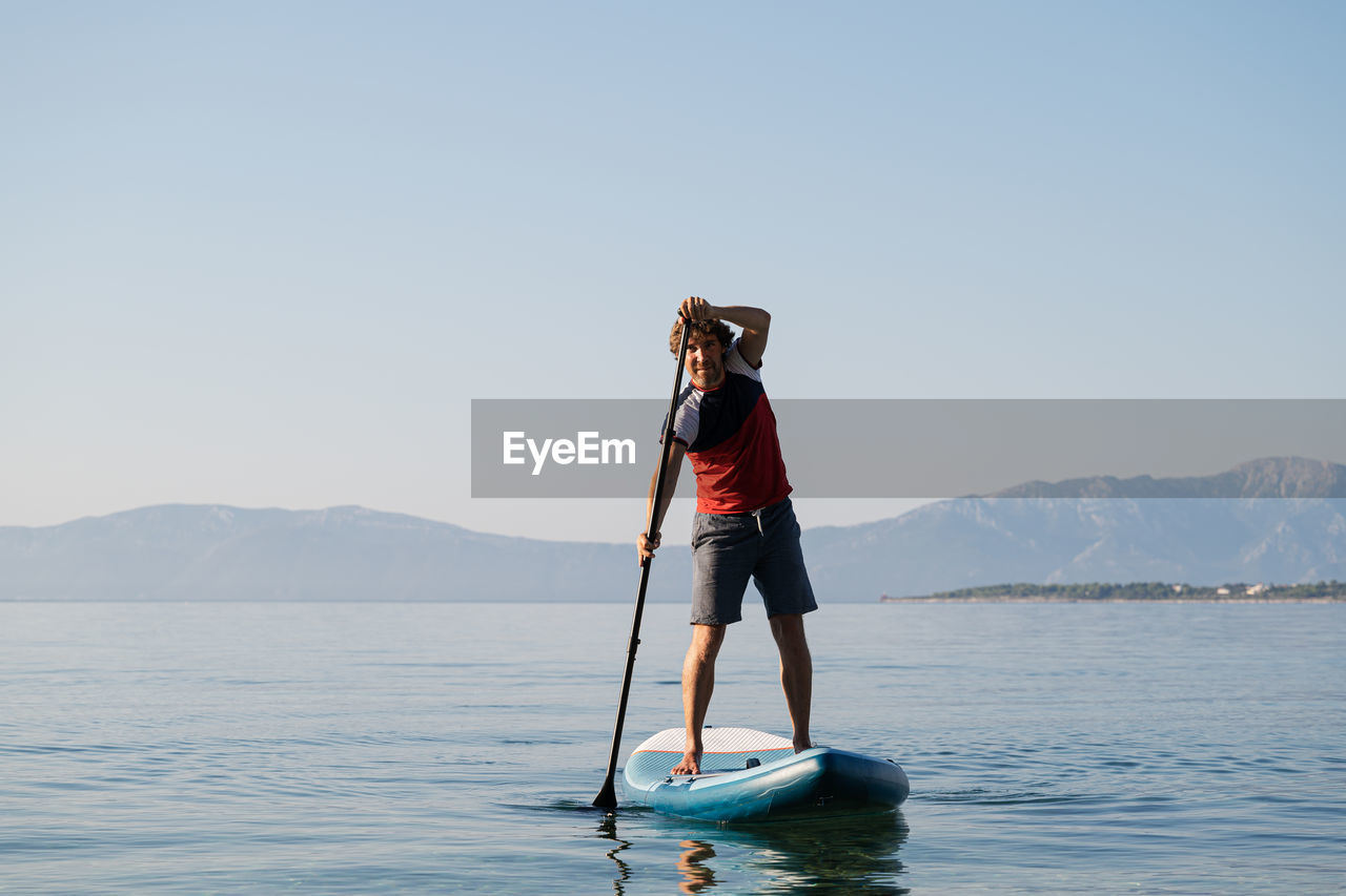 Full length of man paddleboarding in lake against sky