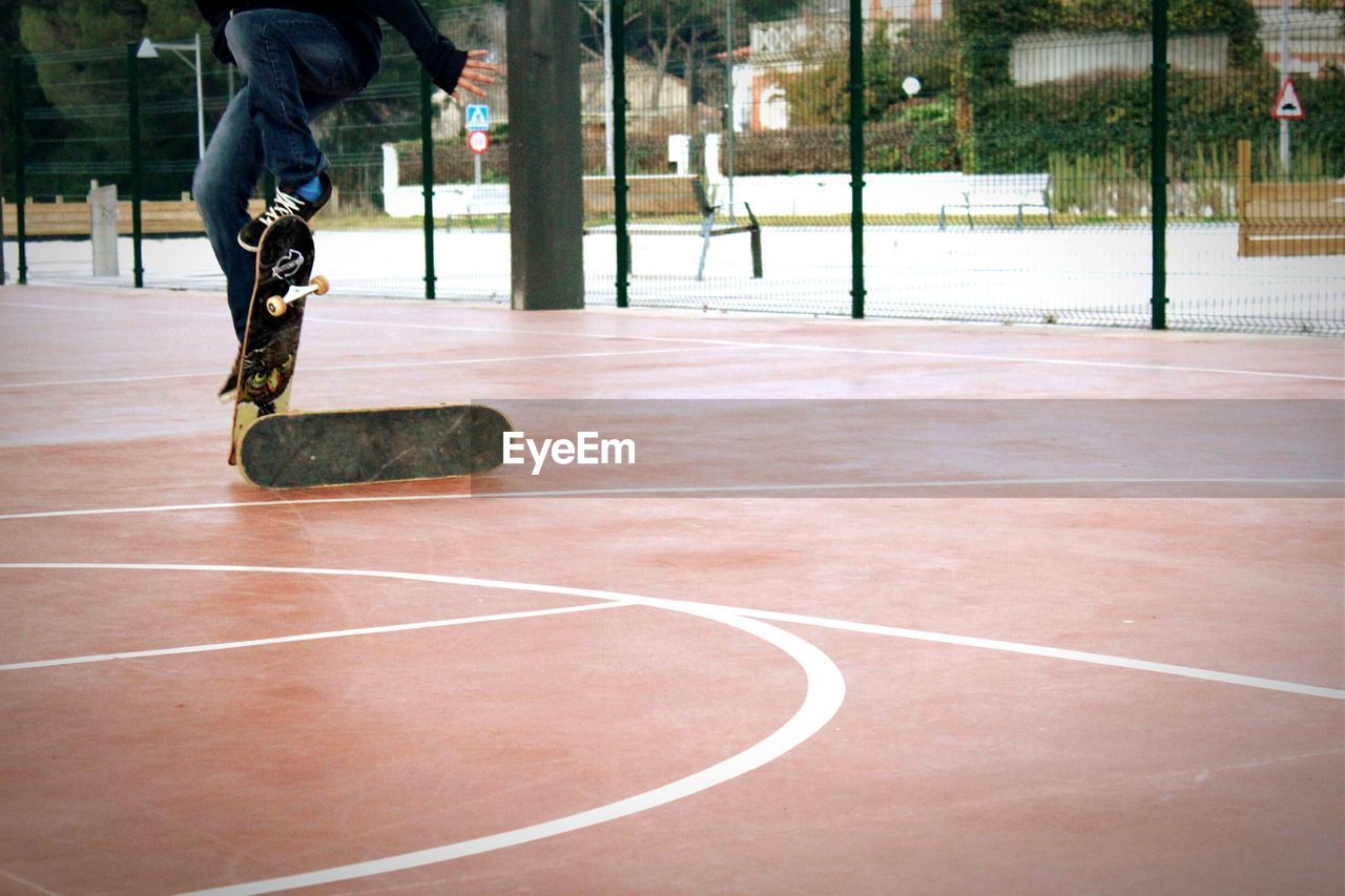 Low section of man performing stunt with skateboard at court