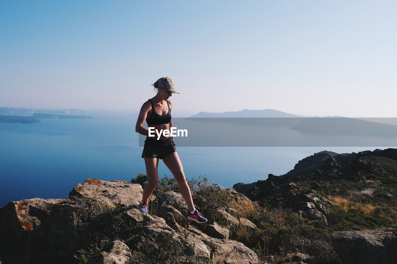 Woman standing on rock by sea against clear sky