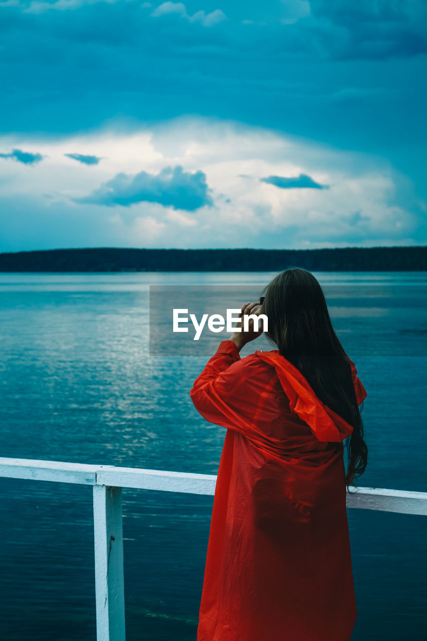 Rear view of woman looking at sea against cloudy sky