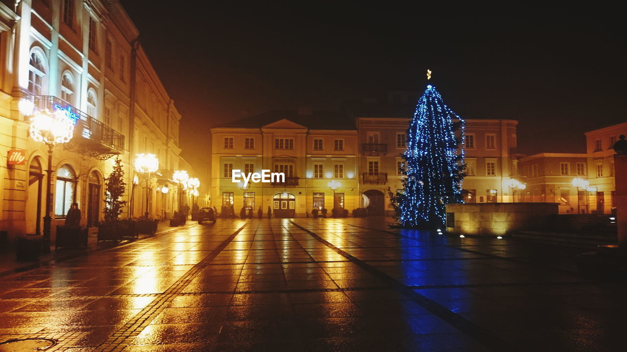 Christmas tree in front of illuminated buildings against clear sky