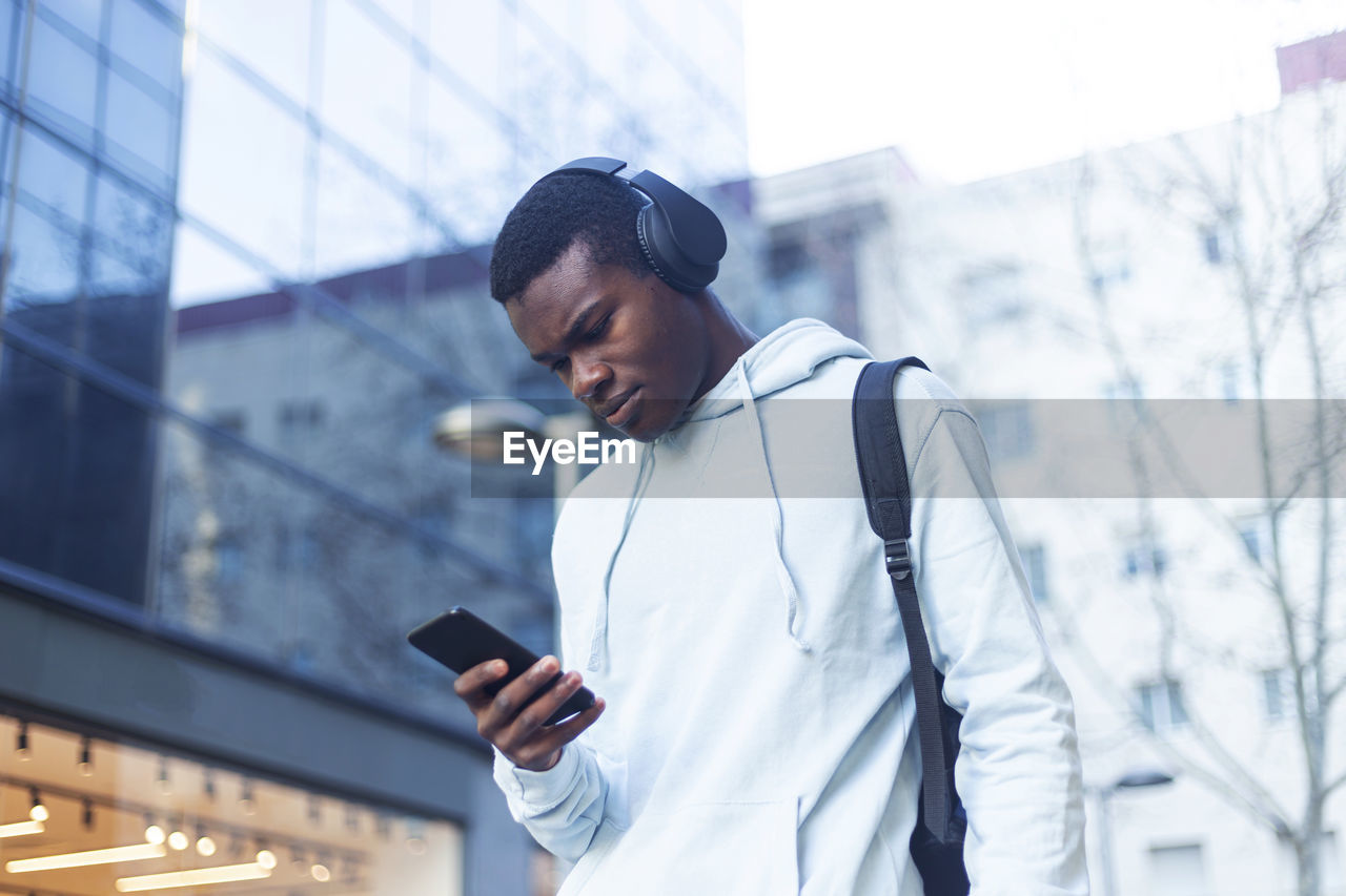 Young man listening to music while using phone outside building