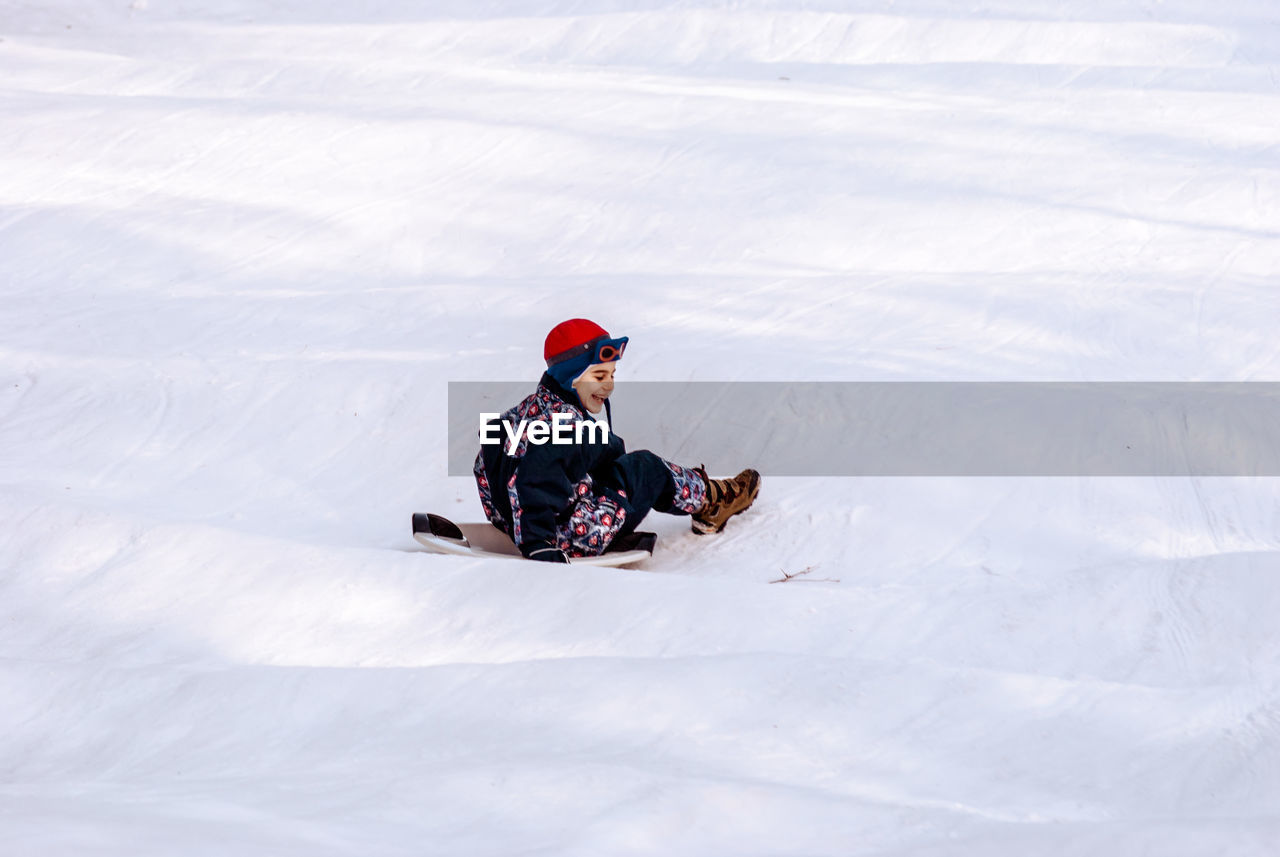 Smiling boy tobogganing on snow covered field during winter
