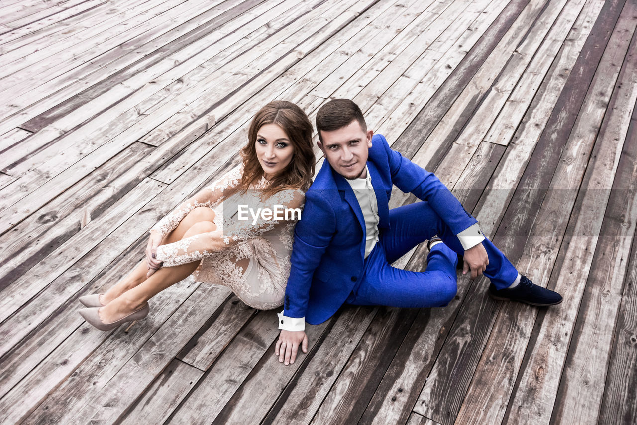 High angle portrait of bride and bridegroom sitting on wooden footpath