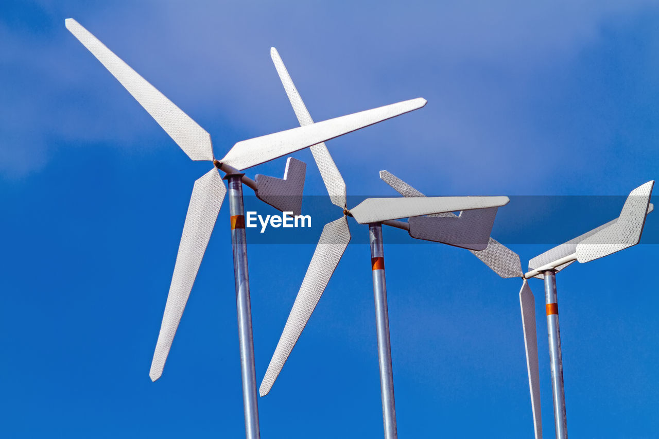 White wind turbines producing alternative energy on blue sky