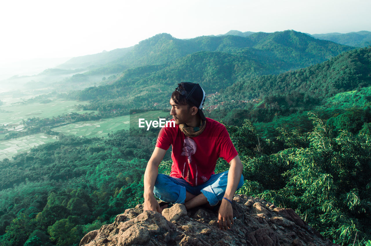 Full length of man sitting on cliff during sunny day