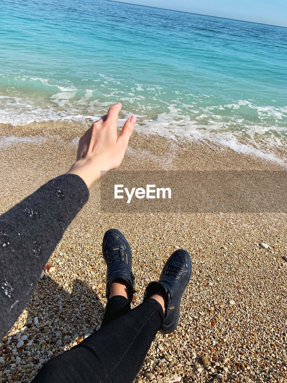 Low section of person gesturing sitting on beach