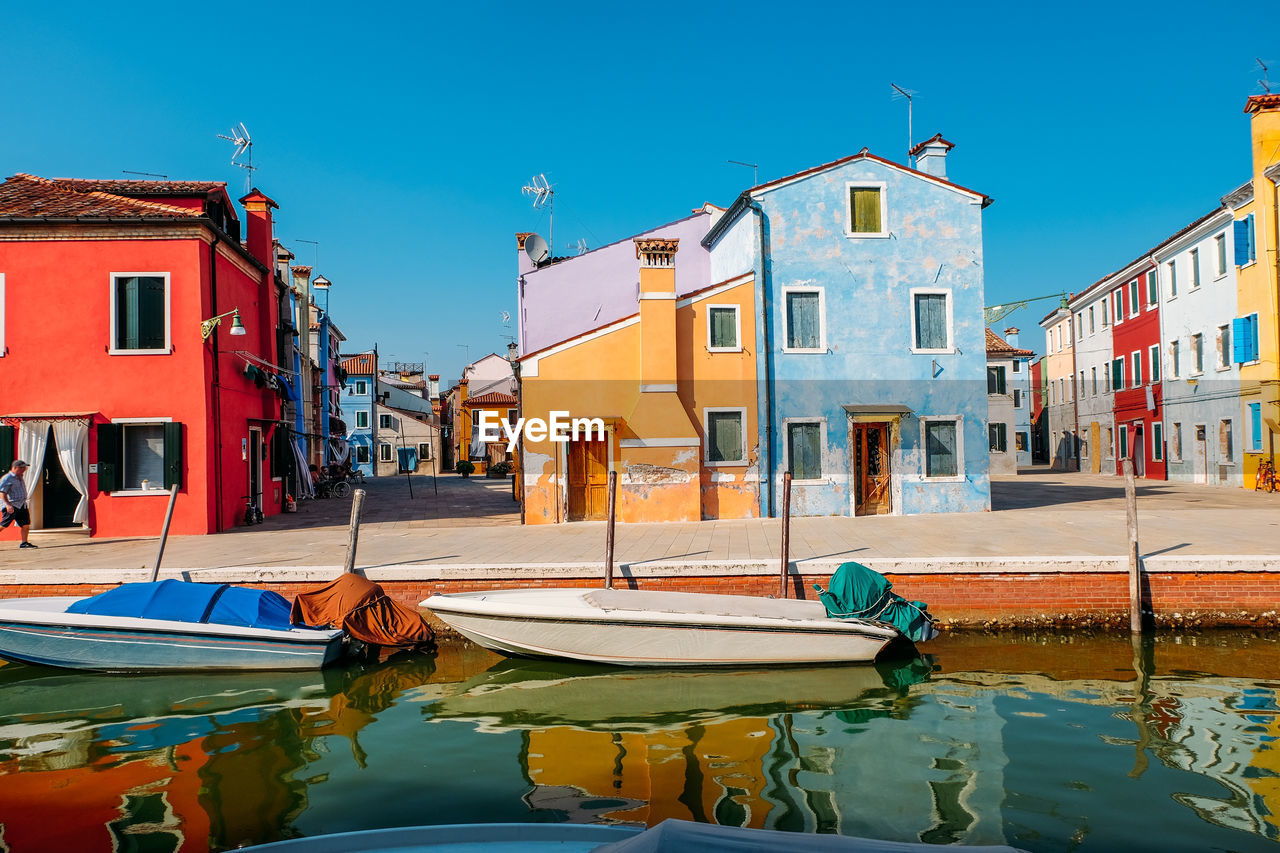 Boats moored in canal by buildings against clear sky