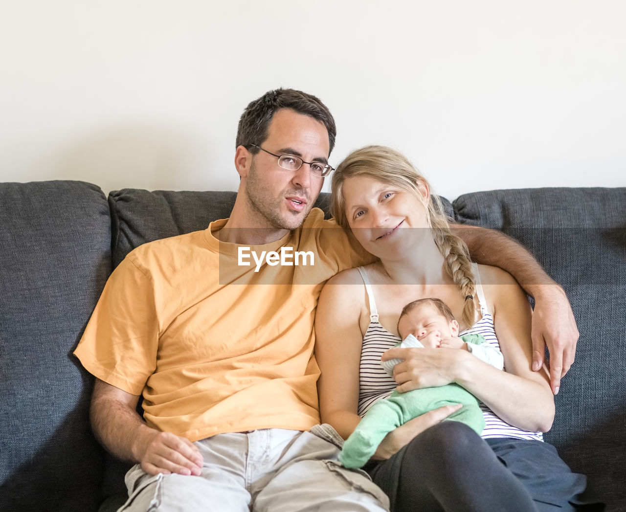 Smiling couple with baby sitting on sofa at home