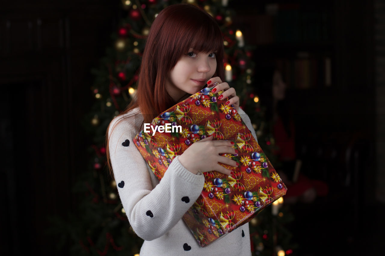 Portrait of young woman holding gift box at home